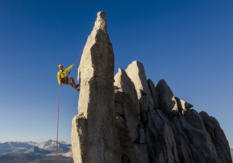 a man in yellow jacket is climbing the rocks